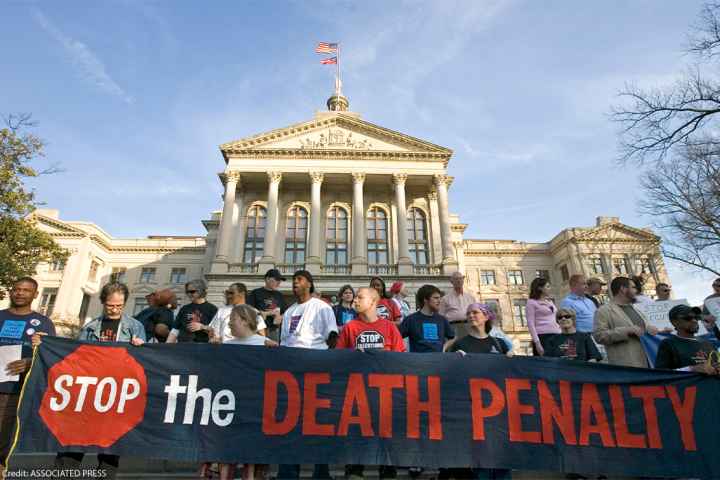 Demonstrators, holding a sign reading "STOP THE DEATH PENALTY", stand on the steps of the State Capitol in Atlanta.