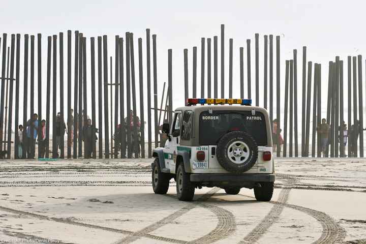 A U.S. Border Patrol vehicle sits parked in front of a crowd of people peering through the U.S.-Mexico border fence in San Diego.