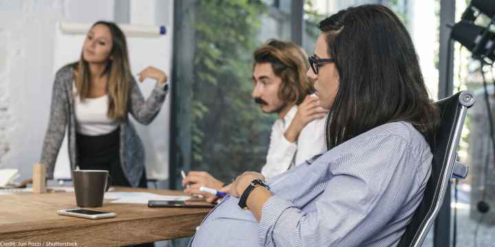 A seated pregnant woman participating in a brainstorming meeting.