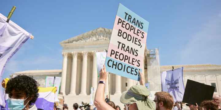 A demonstrator at a march in front of the Supreme Court holds up a sign reading "TRANS PEOPLE'S BODIES, TRANS PEOPLE'S CHOICES".