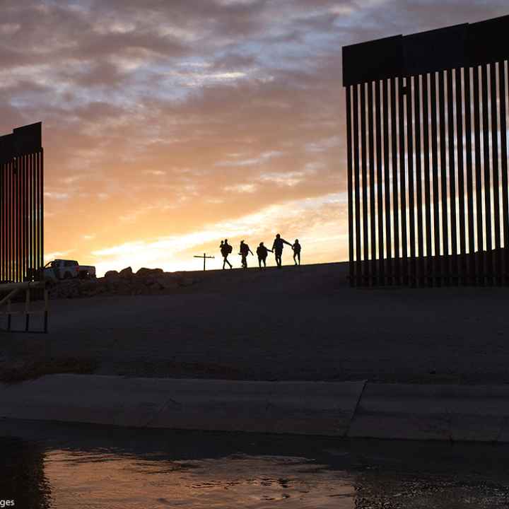 A pair of migrant families at the border wall between the United States and Mexico.