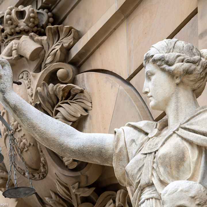 A statue of the goddess Justitia holds a pan of scales in front of the building of the district and regional court.