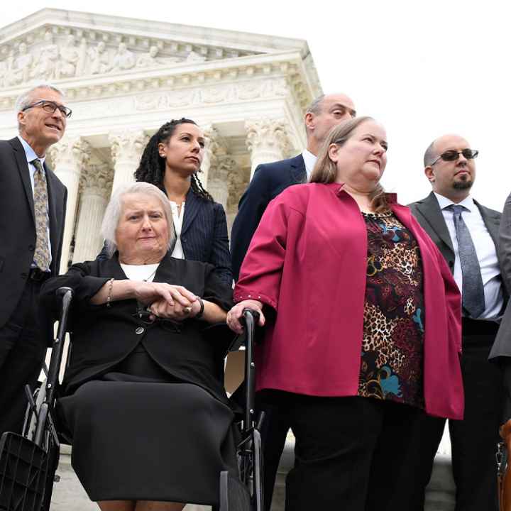 Aimee Stephens, seated, her wife Donna Stephens, in pink, and ACLU attorney Chase Strangio, at the far right listen during a news conference outside the Supreme Court.