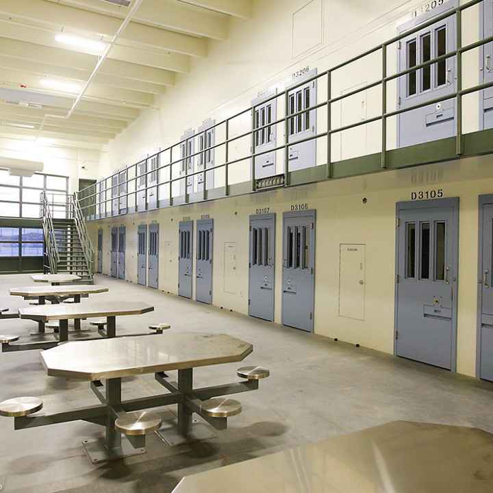 An empty cell block in a prison with tables and blue doors.