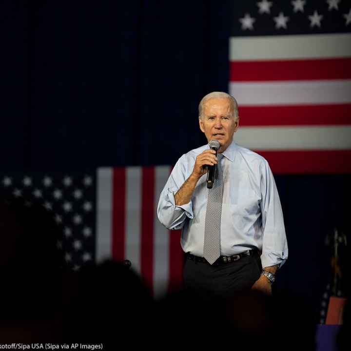 Joe Biden speaking in front of several American flags.