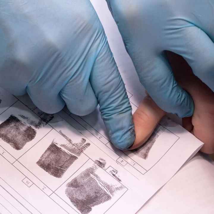 crime investigator wearing gloves fingerprinting person