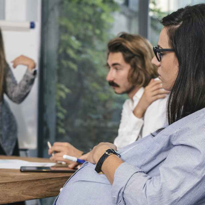 A seated pregnant woman participating in a brainstorming meeting.